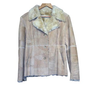 May include: A tan patchwork jacket with a shearling collar and lining, button closure, and two front pockets. The jacket is hanging on a wooden hanger against a white background. The jacket appears to be made of suede or leather.