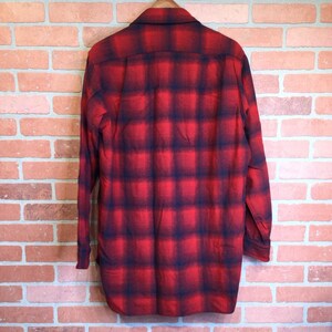 May include: Red and black plaid button-down shirt. The long-sleeved shirt is hanging on a wooden hanger. The plaid pattern is a classic design, with a bold red base and dark blue intersecting lines.