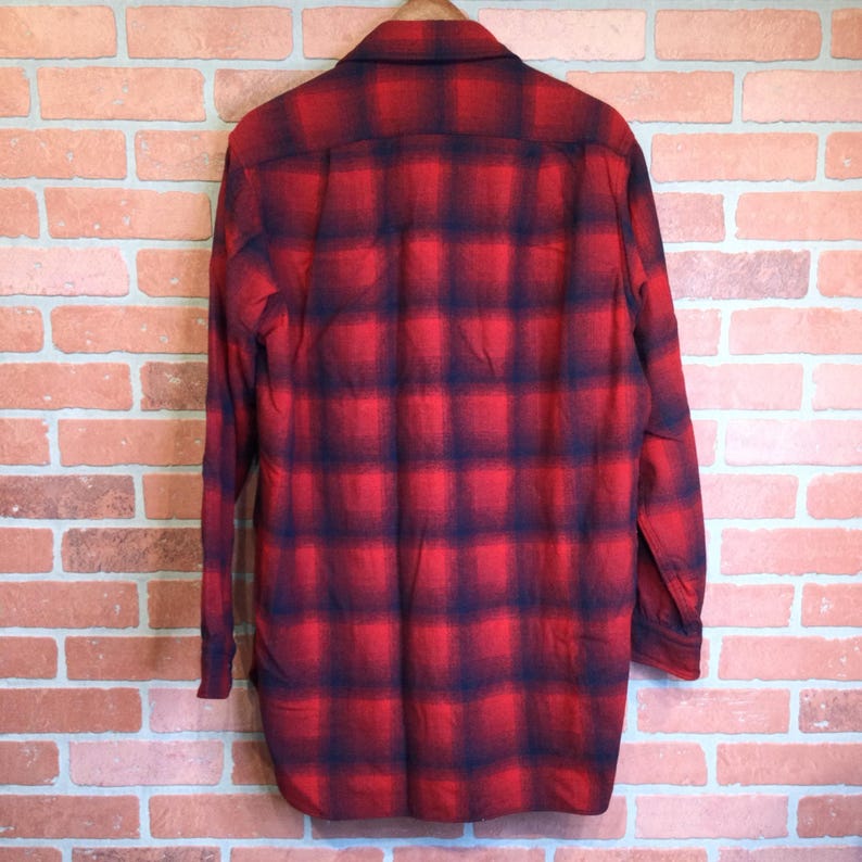 May include: Red and black plaid button-down shirt. The long-sleeved shirt is hanging on a wooden hanger. The plaid pattern is a classic design, with a bold red base and dark blue intersecting lines.