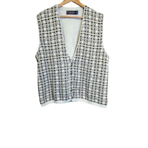 May include: A vintage, button-down vest with a plaid pattern in black, white, and tan. The vest has a V-neck and is made of a knit material. The vest is hanging on a wooden hanger.