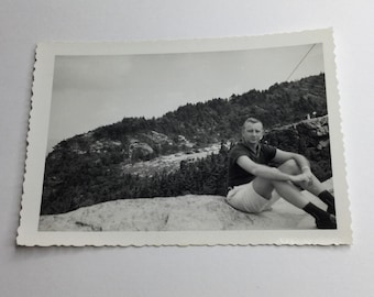 Fotografía vintage en blanco y negro de un hombre apuesto sentado en un paisaje montañoso rocoso.