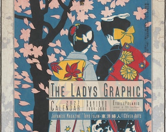 May include: A 2027 wall calendar titled The Ladys Graphic featuring Japanese magazine cover art from 1904-1909. The illustration depicts two figures in traditional attire standing under a cherry blossom tree with pink petals against a blue sky.