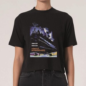 Op de afbeelding: Zwart T-shirt met een filmposterontwerp voor "Edward Scissorhands". De posterkunst bevat een portret van Johnny Depp, de titel van de film en de namen van de acteurs. Het shirt is een cropped style.