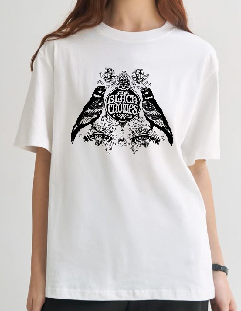 May include: White t-shirt featuring a black graphic design. The design includes two crows flanking a circular emblem with the text "THE BLACK CROWES" and the words "HARD TO HANDLE" below. The shirt has short sleeves.