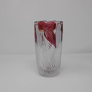 May include: A clear glass vase with a textured, ribbed design. The vase has a red floral design around the top.