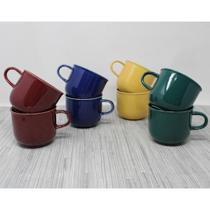 May include: A collection of six ceramic mugs in various colors: burgundy, navy blue, yellow, and dark green. Each mug has a rounded body, a curved handle, and a glossy finish. The mugs are stacked in pairs.