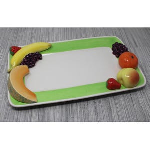 Peut inclure: Un plat de service rectangulaire blanc avec une bordure verte. Le plat est décoré de divers fruits, dont une banane, un cantaloup, une orange, une pomme et des fraises.