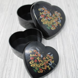 May include: Two black heart-shaped boxes with floral designs. The top box is open and the bottom box is closed.