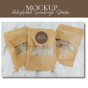 May include: Three brown paper pouches with a clear window, filled with dehydrated sourdough starter. The pouches are on a white fluffy surface. One pouch has a brown circle label with the text "DIGITAL PRODUCT".
