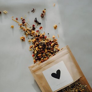 Könnte beinhalten: Ein brauner Papierbeutel gefüllt mit losen Blättern Tee. Der Tee ist eine Mischung aus getrockneten Früchten, Kräutern und Blüten. Der Beutel hat ein weißes Etikett mit einem schwarzen Herzen und dem Text "Whimsiberry".