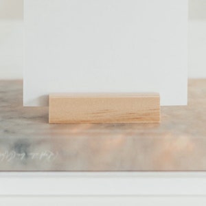 May include: A white card is propped up on a wooden block, which is sitting on a marble surface.