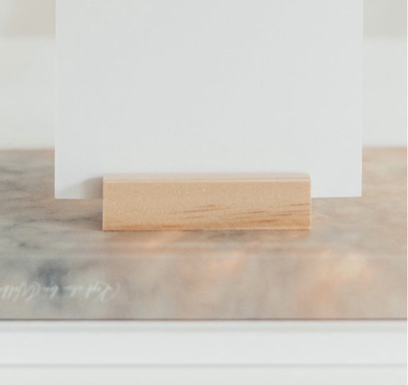 May include: A white card is propped up on a wooden block, which is sitting on a marble surface.