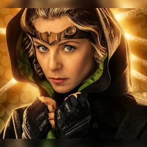 May include: A woman with blonde hair and blue eyes, wearing a dark hooded cloak with green trim and a gold headpiece. The background features a golden, clock-like design with radiating lines.
