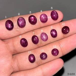 Peut inclure: Treize rubis étoilés ovales de couleur magenta profond, disposés en rangées et numérotés de 1 à 13 en blanc. Ces pierres précieuses polies présentent un effet d'étoile à six branches distinct sur leurs surfaces, avec une teinte riche et saturée.