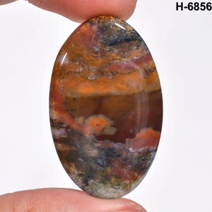 May include: An oval-shaped gemstone with a polished surface. The stone features a blend of colors, including orange, brown, red, and gray, with a marbled appearance. The text "H-6856" is visible in the upper right corner.