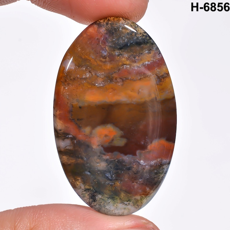 May include: An oval-shaped gemstone with a polished surface. The stone features a blend of colors, including orange, brown, red, and gray, with a marbled appearance. The text "H-6856" is visible in the upper right corner.