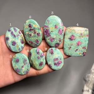 Puede incluir: Siete piedras preciosas pulidas con una base de color turquesa e inclusiones rojas vibrantes. Las piedras varían en forma, incluyendo ovaladas y rectangulares. Las piedras preciosas se sostienen en una mano. El texto "B116" es visible en la esquina inferior derecha.