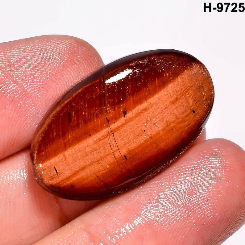 May include: An oval-shaped, polished gemstone in shades of reddish-brown, exhibiting a chatoyant effect. The stone's surface is smooth and glossy, with visible banding and inclusions. The text "H-9725" is visible in the upper right corner.