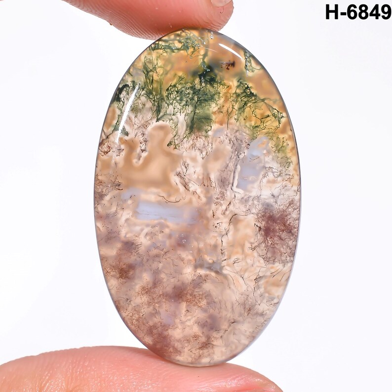 May include: Oval-shaped moss agate gemstone with a polished surface. The stone features a blend of colors, including green, brown, beige, and hints of purple. The text "H-6849" is visible in the upper right corner.
