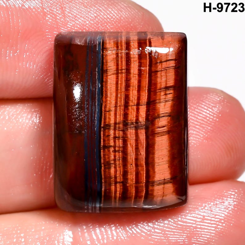 May include: A rectangular gemstone with a polished surface. The stone features a mix of reddish-brown and dark blue colours, with a striped pattern. The text "H-9723" is visible in the upper right corner.