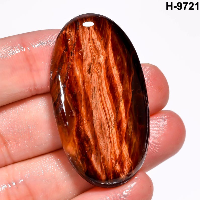 May include: An oval gemstone with a polished surface. The stone has a rich, warm brown colour with intricate, swirling patterns resembling wood grain. The gemstone is held in a hand against a white background. The text "H-9721" is in the upper right corner.