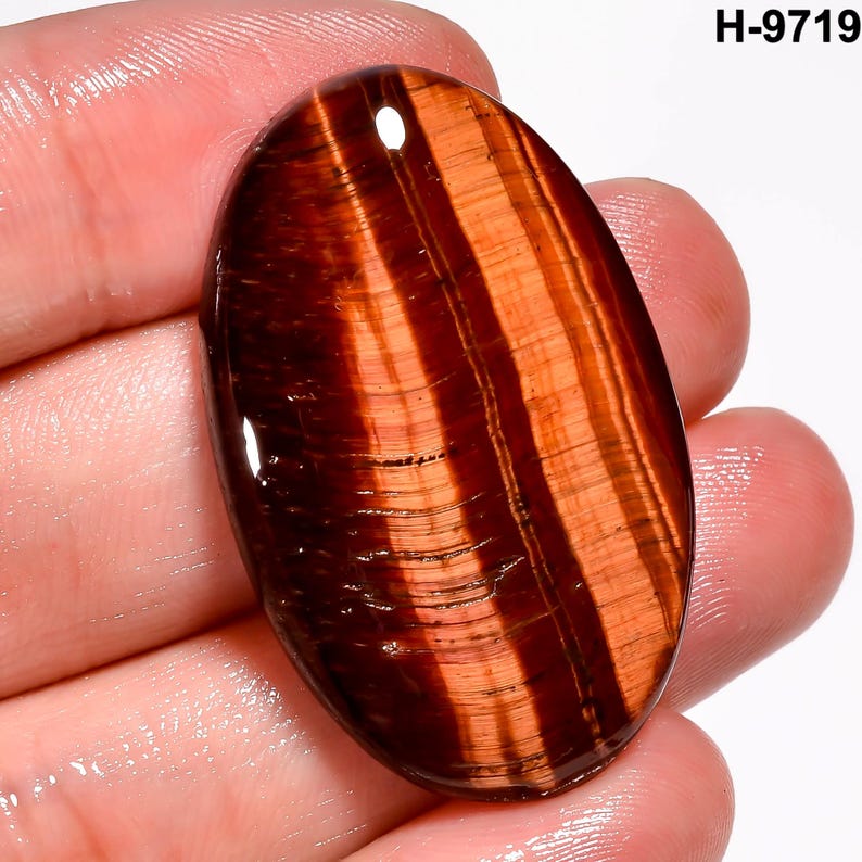 May include: An oval gemstone with a polished surface. The stone displays a pattern of parallel bands in shades of reddish-brown and orange. The gemstone is held in a hand, and the text "H-9719" is visible in the upper right corner.