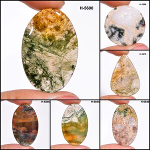 May include: A collection of polished gemstones in various shapes, including oval, round, and teardrop. The stones display a range of colors, such as green, brown, white, and orange, with unique patterns and textures. Each stone has a product code.
