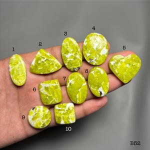May include: A collection of ten polished gemstones in various shapes, including oval, triangular, square, and heart. The stones are a vibrant yellow-green color with white veining. The gemstones are numbered 1 through 10.