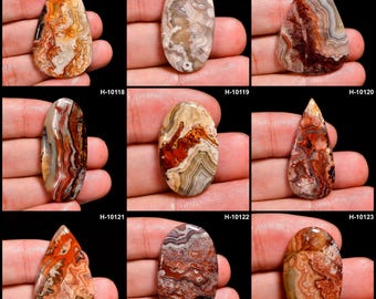 May include: Nine polished agate gemstones in various shapes, including oval and teardrop. The stones display a range of colors, such as orange, brown, red, and cream, with intricate banding patterns. Each stone is held in a hand against a black background.