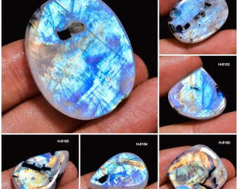 May include: A collection of polished moonstone gemstones in various shapes. The stones display a mix of blue, white, and iridescent colors, with internal patterns and inclusions. Each stone is held in a hand, showcasing the natural beauty and unique characteristics of each piece.