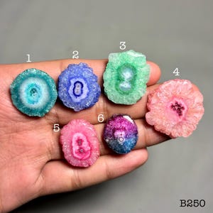 May include: Six polished solar quartz geodes in various colours, including blue, green, pink, and purple. Each geode has a central crystalline structure. The image includes the text "B250".
