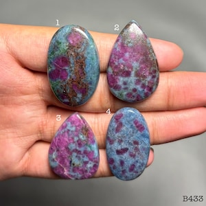 Può includere: Quattro pietre preziose lucide di varie forme, tra cui ovali e a goccia. Le pietre presentano un colore di base blu-verde con inclusioni rosse e marroni. Le pietre sono tenute in una mano. Il testo "B433" è visibile in basso a destra.