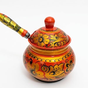 May include: A round wooden pot with a lid and a long handle, featuring a vibrant red and gold floral pattern painted across the entire surface. The design includes intricate black line work detailing the petals and leaves on the exterior.