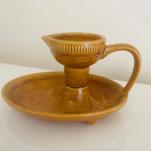 May include: A brown ceramic candle holder with a small dish and a handle. The holder has a textured surface and a simple design.