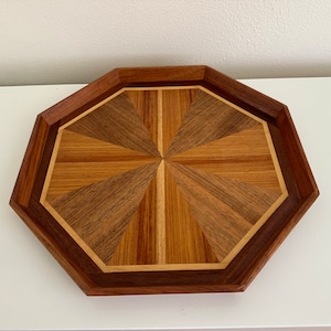 May include: Octagonal wooden tray with a geometric inlay design. The tray is made of dark wood with a light wood border.