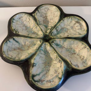 May include: A green and white ceramic oyster plate with six individual sections. The plate is shaped like a flower with a raised centre.
