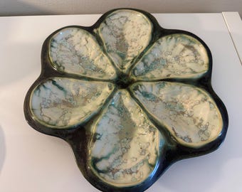 May include: A green and white ceramic oyster plate with six individual sections. The plate is shaped like a flower with a raised center.