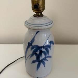 May include: A white ceramic table lamp with a blue bamboo design. The lamp has a brass socket and a white cord.