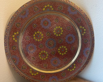 May include: A round brass tray with a red background and intricate gold and multi-colored floral designs.