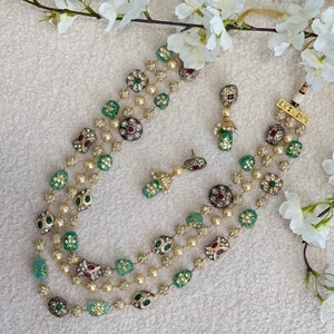 May include: A three-strand necklace with green and red gemstone beads, gold accents, and pearl accents. Matching earrings with green and red gemstones are included.