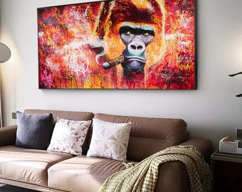 May include: A large framed canvas art piece featuring a gorilla smoking a cigar. The artwork uses vibrant colors, with a focus on red, orange, and yellow hues. The gorilla's face is detailed, with a serious expression. The artwork is displayed above a brown sofa.