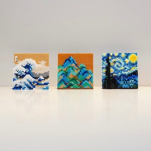 May include: Three small framed pixel art pieces depicting famous paintings. The first piece is a blue and white rendition of "The Great Wave off Kanagawa". The second piece is a green and blue rendition of "Starry Night" by Vincent van Gogh. The third piece is a blue and yellow rendition of "The Scream" by Edvard Munch.