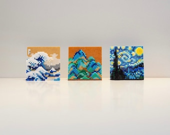 May include: Three small framed pixel art pieces depicting famous paintings. The first piece is a blue and white rendition of "The Great Wave off Kanagawa". The second piece is a green and blue rendition of "Starry Night" by Vincent van Gogh. The third piece is a blue and yellow rendition of "The Scream" by Edvard Munch.