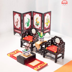 Puede incluir: Un conjunto de sala de estar en miniatura hecho de cuentas de plástico de colores. El conjunto incluye dos sillas, una mesa, una alfombra y una pantalla. Las sillas y la mesa son negras con cojines rojos. La alfombra es roja con detalles amarillos. La pantalla está hecha de cuatro paneles con diferentes diseños florales.