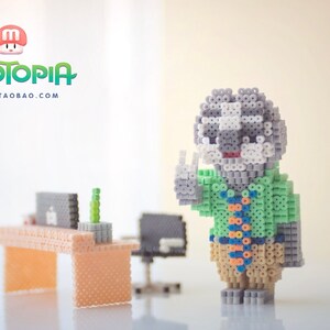 May include: A gray and white bead figurine of a character from the movie Zootopia, wearing a green shirt and a tie. The figurine is standing on a white surface with a desk and chair in the background. The text "Zootopia" and "MARD.TAOBAO.COM" is visible in the top left corner of the image.
