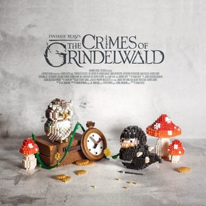 Peut inclure: Gros plan sur une scène miniature du film "Les Animaux fantastiques : Les Crimes de Grindelwald". La scène représente une valise brune, une horloge, un champignon et un petit hibou en perles colorées.