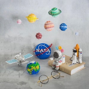 May include: A colorful space-themed set of miniature models, including planets, a rocket, a satellite, an astronaut, and a globe. The set also includes a blue circle with the word "NASA" in white letters.