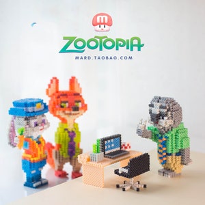 May include: A set of three Zootopia character figurines made of colourful plastic beads. The characters are Judy Hopps, Nick Wilde, and Flash. The figurines are standing in front of a small desk with a computer and chair. The text "Zootopia" and "mard.taobao.com" is visible in the background.