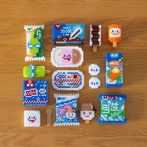 May include: A collection of 14 colorful pixel art ice cream treats and snacks. The treats are made of small plastic beads and feature various designs, including a snowman, a penguin, and a popsicle.