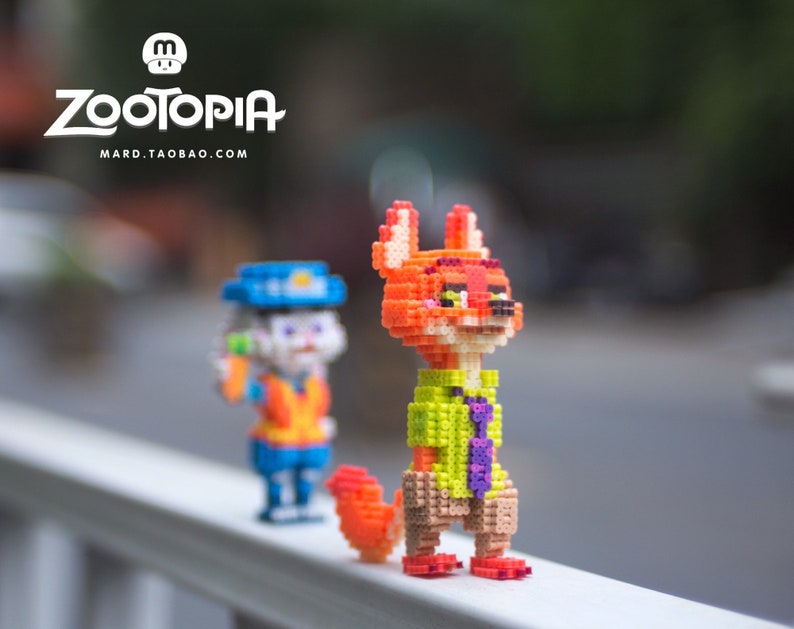 May include: Two small, colorful, pixelated figurines of characters from the movie Zootopia. The figurine on the left is a bunny wearing a police uniform and holding a carrot. The figurine on the right is a fox wearing a green shirt and a purple tie. The figurines are standing on a white railing.